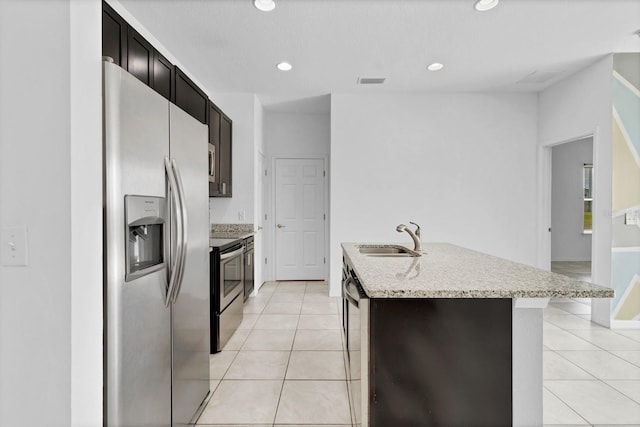 kitchen featuring light tile patterned floors, stainless steel appliances, an island with sink, and a sink