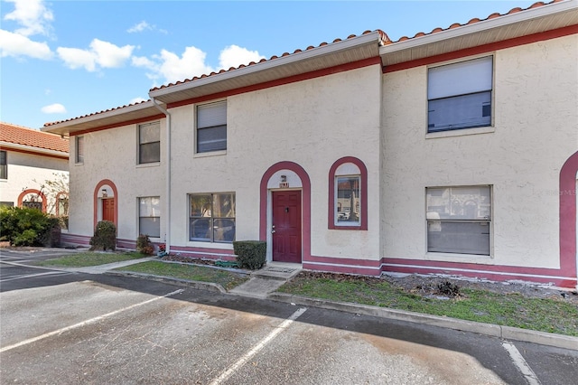 multi unit property with uncovered parking, a tiled roof, and stucco siding