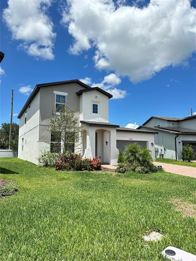 view of front facade with a garage, driveway, a front yard, and stucco siding