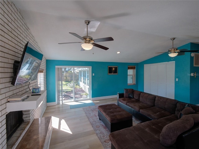 living area with lofted ceiling, light wood-style floors, a ceiling fan, a brick fireplace, and baseboards