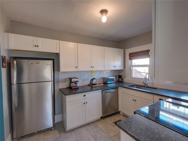 kitchen featuring tasteful backsplash, dark stone counters, stainless steel appliances, white cabinetry, and a sink