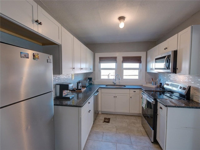 kitchen featuring stainless steel appliances, tasteful backsplash, white cabinets, a sink, and dark stone countertops