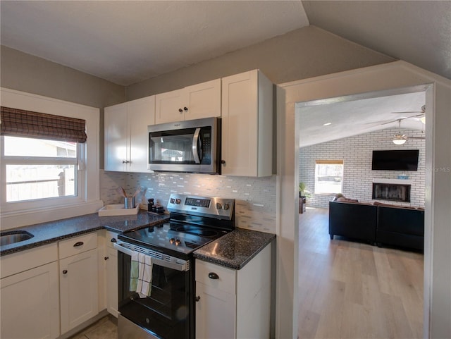 kitchen with stainless steel appliances, white cabinets, vaulted ceiling, a brick fireplace, and decorative backsplash