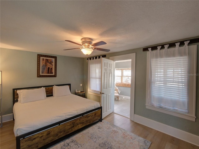 bedroom with light wood-style flooring, a textured ceiling, baseboards, and a ceiling fan