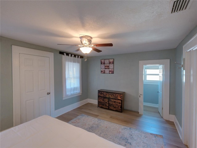 bedroom with a textured ceiling, wood finished floors, visible vents, and baseboards