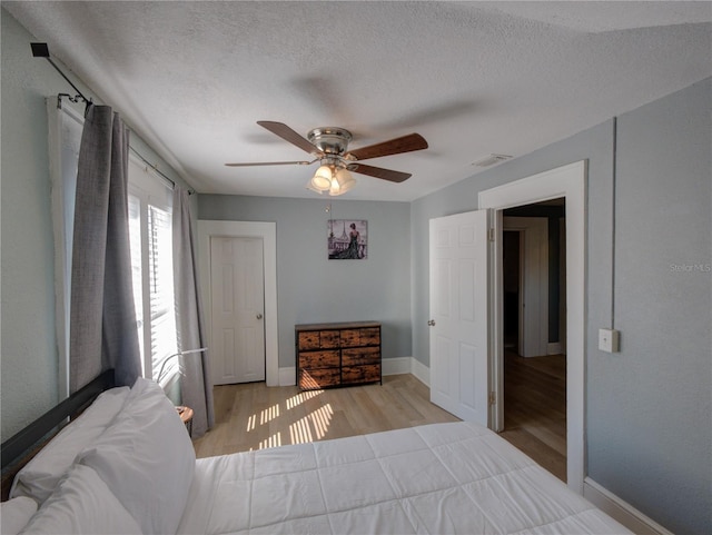 bedroom with a textured ceiling, wood finished floors, visible vents, and baseboards