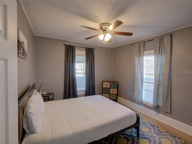 bedroom with a textured ceiling, wood finished floors, a ceiling fan, and baseboards