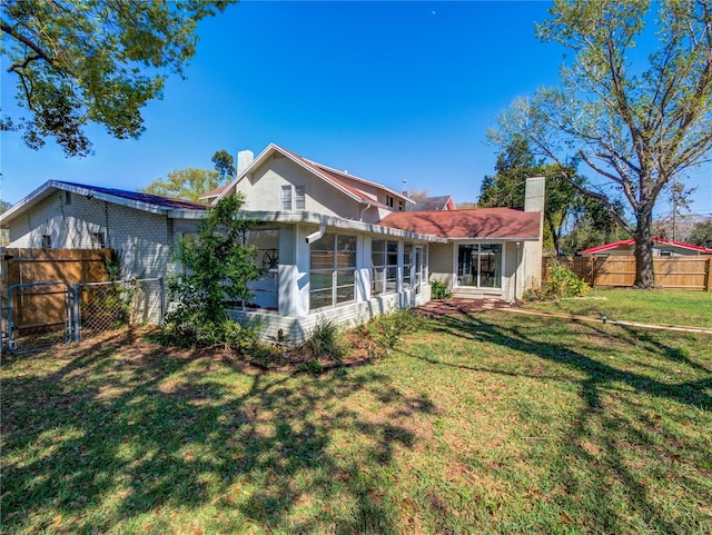 rear view of house with a sunroom, a fenced backyard, a chimney, and a yard