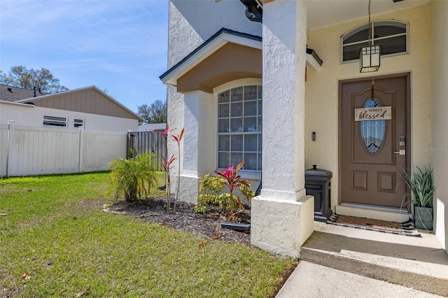 property entrance with a yard, fence, and stucco siding