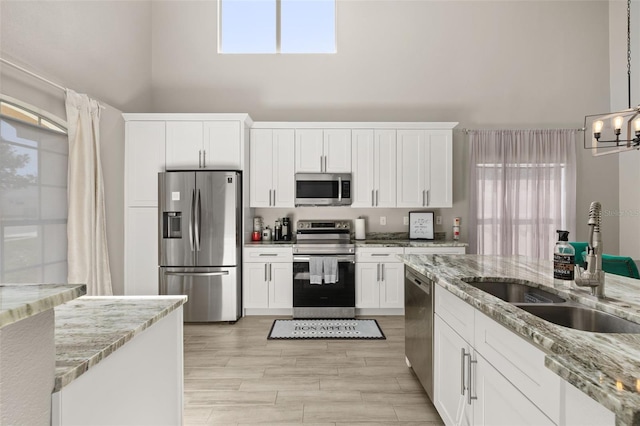 kitchen featuring a towering ceiling, appliances with stainless steel finishes, white cabinets, and a sink