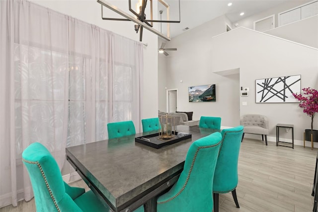 dining space featuring ceiling fan, wood finished floors, visible vents, a towering ceiling, and baseboards