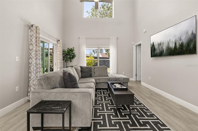 living area with a towering ceiling, baseboards, and wood finished floors