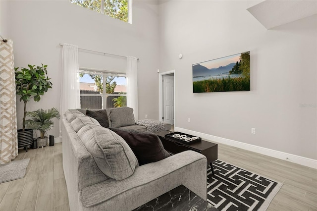 living area featuring light wood finished floors, a high ceiling, and baseboards