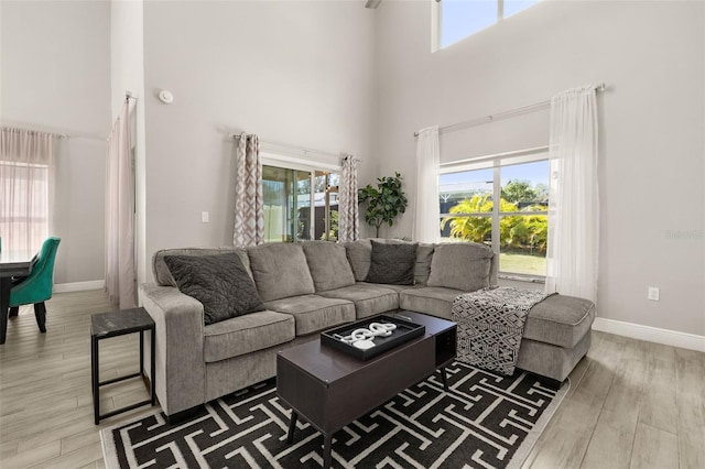 living room with a towering ceiling, a wealth of natural light, baseboards, and wood finished floors