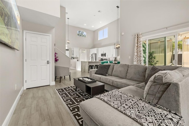 living room with a towering ceiling, light wood finished floors, baseboards, and recessed lighting