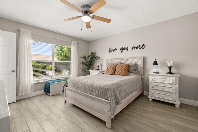 bedroom with light wood-type flooring, ceiling fan, baseboards, and a textured ceiling