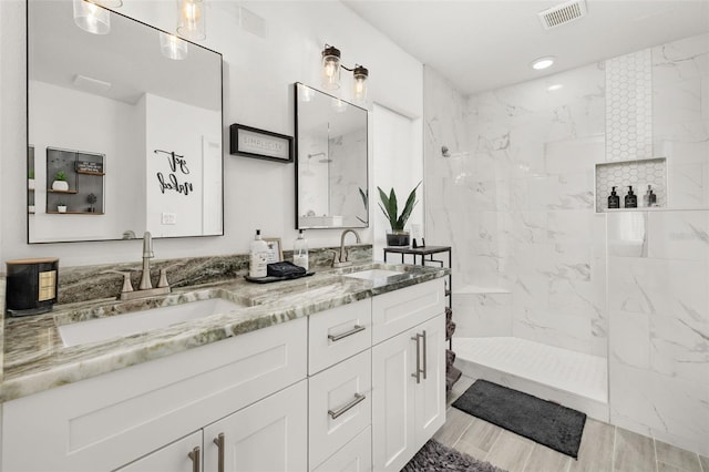 bathroom featuring visible vents, a sink, a marble finish shower, and double vanity