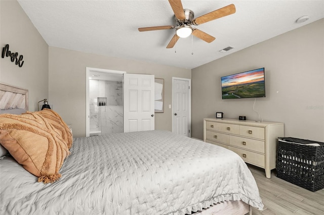 bedroom featuring light wood-style flooring, ensuite bath, visible vents, and a ceiling fan