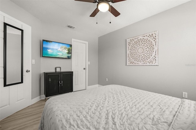 bedroom featuring a ceiling fan, visible vents, baseboards, and wood finished floors