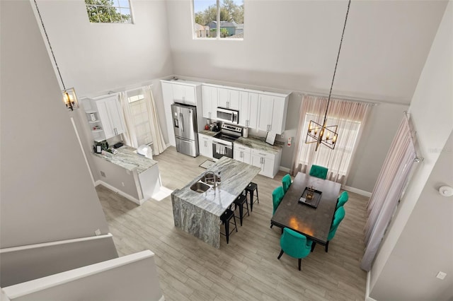 dining space featuring baseboards, a notable chandelier, light wood-style flooring, and a high ceiling