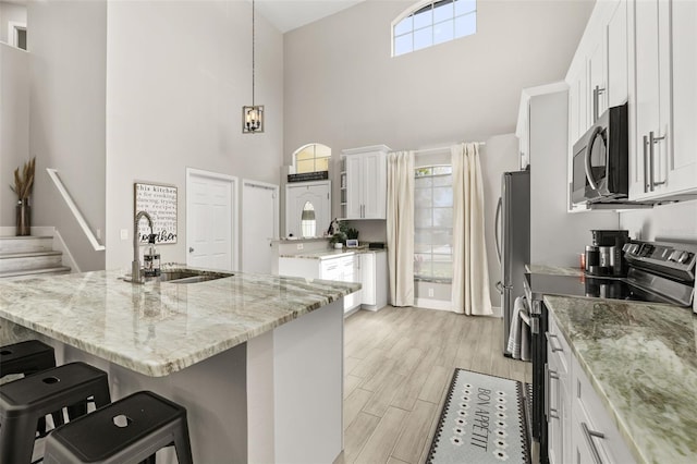 kitchen with a sink, white cabinetry, appliances with stainless steel finishes, light wood-type flooring, and a kitchen bar