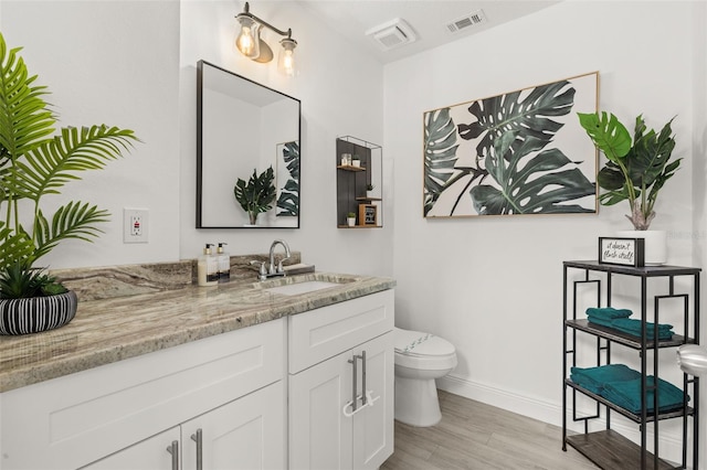 bathroom with toilet, wood finished floors, visible vents, vanity, and baseboards