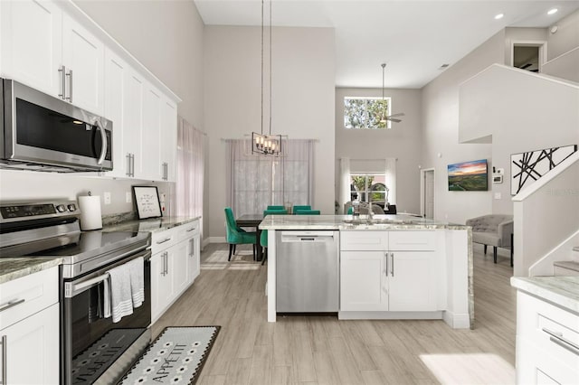 kitchen featuring light wood finished floors, stainless steel appliances, a towering ceiling, white cabinetry, and a chandelier