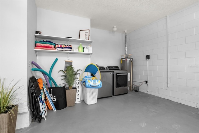 interior space with water heater, a textured ceiling, washing machine and clothes dryer, and concrete block wall