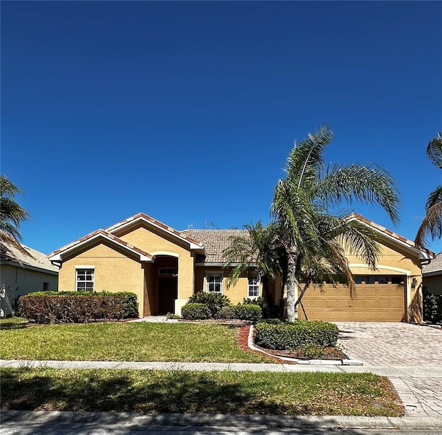 view of front facade featuring an attached garage, a tile roof, decorative driveway, stucco siding, and a front lawn