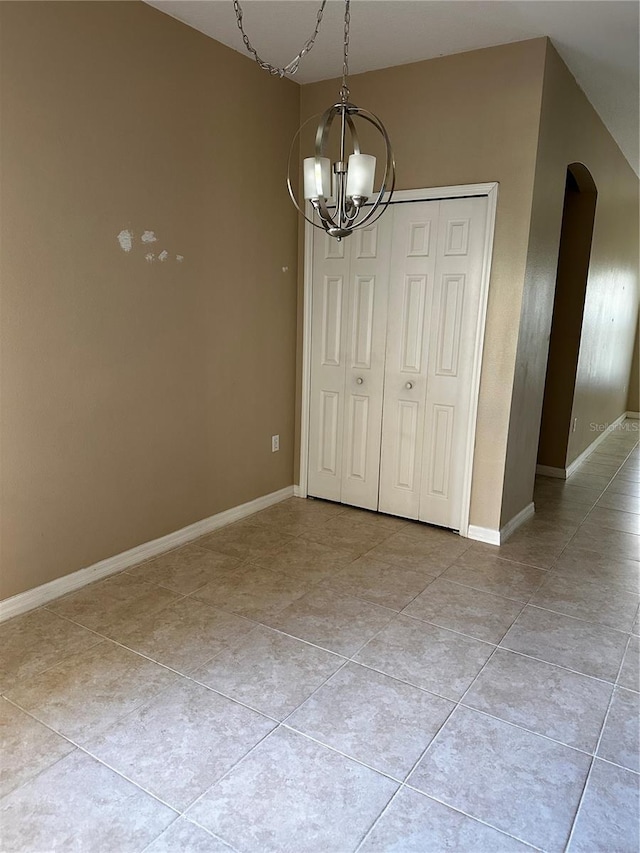 unfurnished dining area with baseboards, arched walkways, a notable chandelier, and light tile patterned flooring