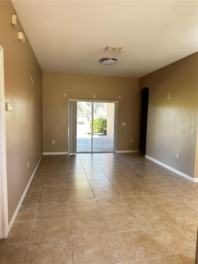 empty room with arched walkways, a textured ceiling, light tile patterned flooring, and baseboards