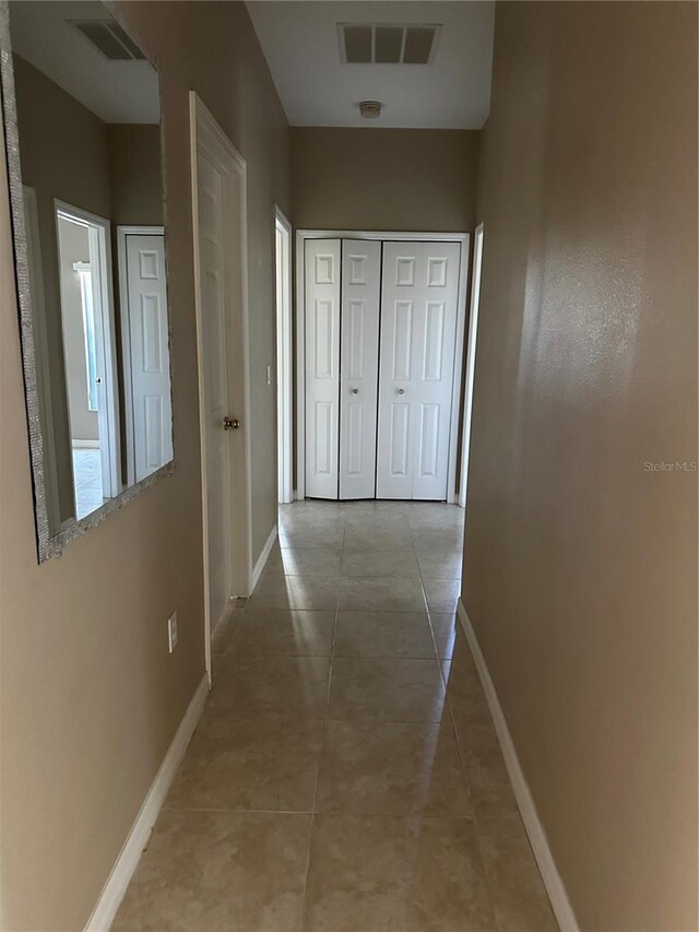 hall with light tile patterned flooring, visible vents, and baseboards