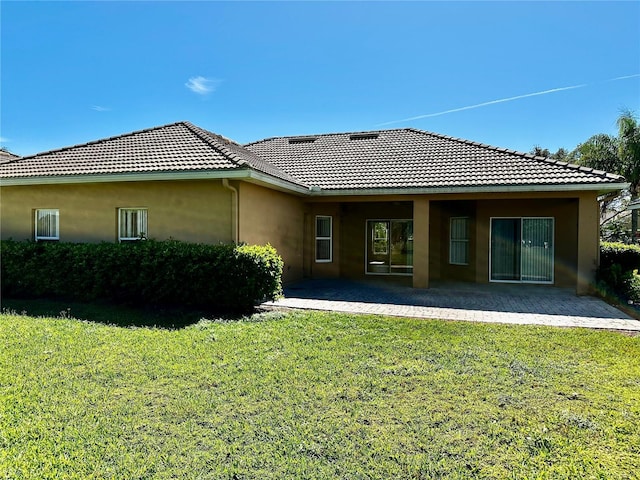 back of property featuring a yard, a patio area, a tiled roof, and stucco siding