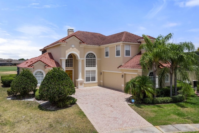 mediterranean / spanish-style house with decorative driveway, a chimney, stucco siding, a front yard, and a tiled roof