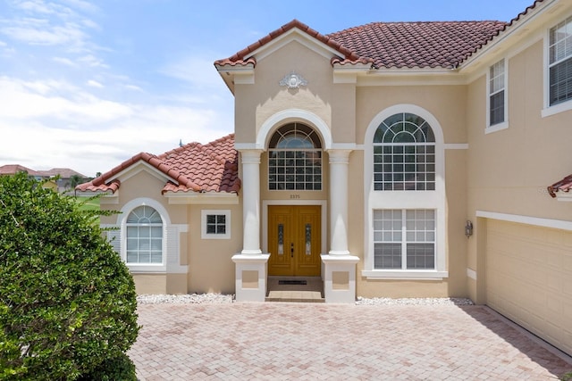 mediterranean / spanish-style house with a garage, a tile roof, driveway, and stucco siding