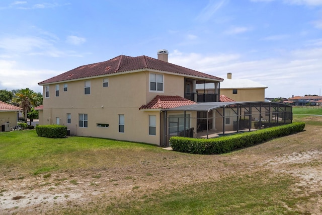 back of property with a lawn, a balcony, glass enclosure, a chimney, and a tiled roof