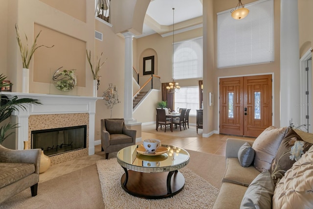 tiled living room with decorative columns, a notable chandelier, a towering ceiling, a tiled fireplace, and baseboards