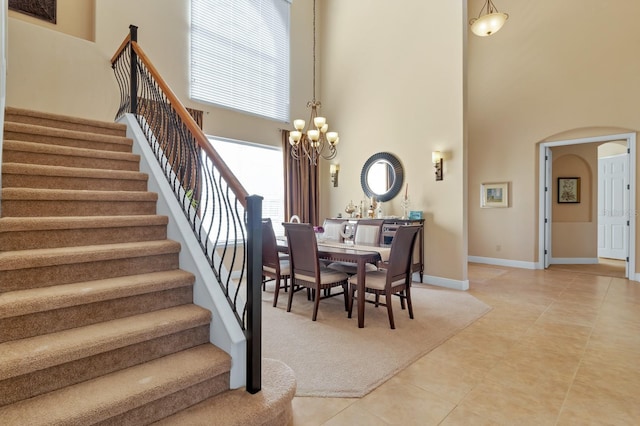 dining space featuring arched walkways, light tile patterned floors, a notable chandelier, a high ceiling, and stairs