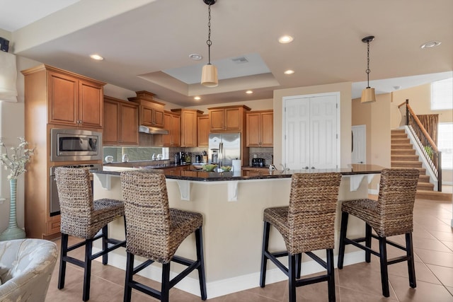 kitchen with a breakfast bar, a tray ceiling, visible vents, decorative backsplash, and appliances with stainless steel finishes