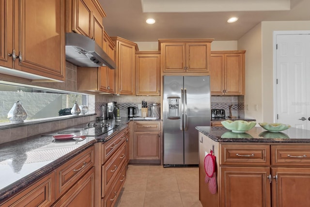 kitchen featuring stainless steel fridge, tasteful backsplash, dark stone counters, under cabinet range hood, and light tile patterned flooring