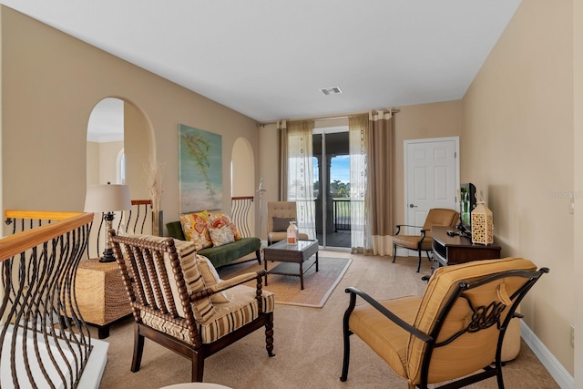 living area featuring arched walkways, light carpet, visible vents, and baseboards