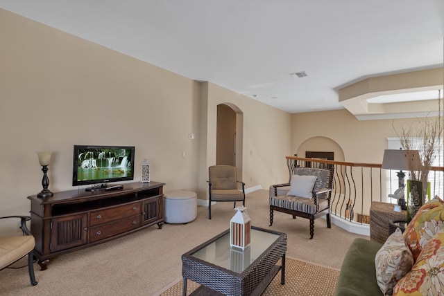 living area featuring arched walkways, visible vents, light carpet, and baseboards