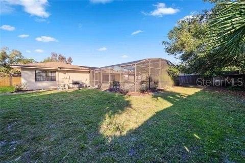 rear view of house with glass enclosure, fence, and a lawn