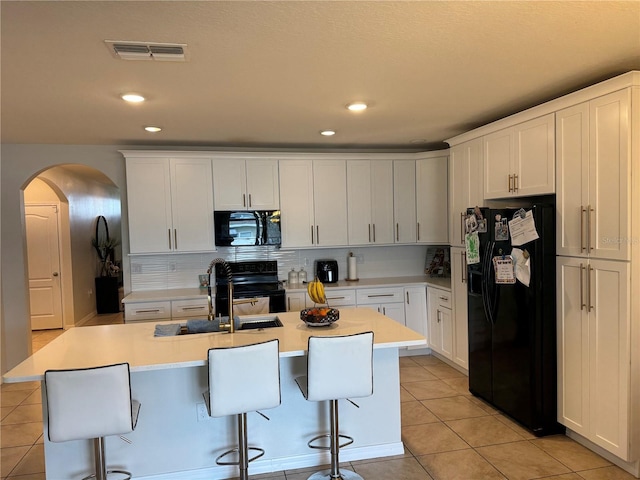 kitchen featuring arched walkways, a breakfast bar area, light countertops, light tile patterned flooring, and black appliances