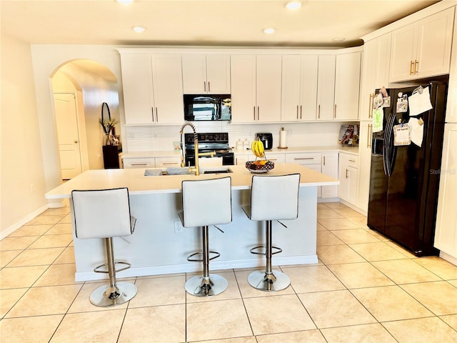 kitchen featuring light tile patterned floors, black appliances, arched walkways, and a kitchen bar