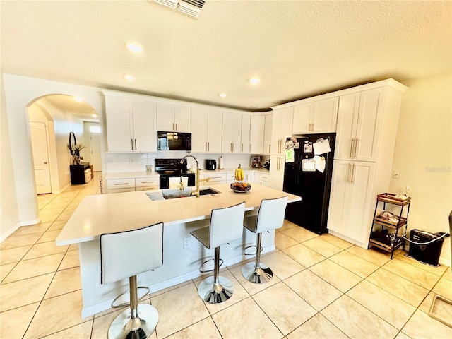 kitchen featuring visible vents, black appliances, a sink, arched walkways, and light tile patterned floors