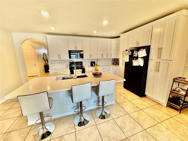 3082 Royal Tern Dr, Winter Haven, FL 33881 - kitchen with black appliances, arched walkways, white cabinetry, light countertops, and recessed lighting