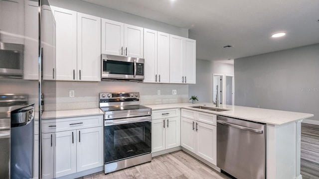 kitchen with light wood-style flooring, a peninsula, a sink, white cabinets, and appliances with stainless steel finishes