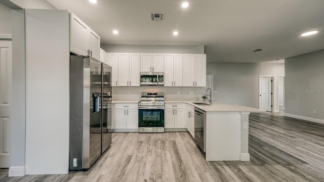 kitchen featuring visible vents, a peninsula, stainless steel appliances, light wood-style floors, and a sink