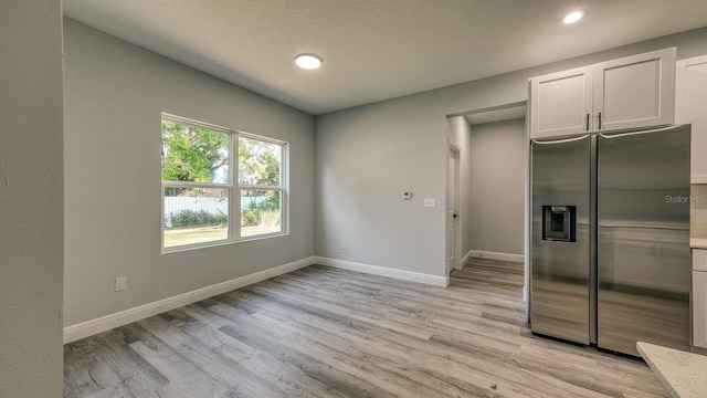 kitchen with baseboards, light countertops, light wood-type flooring, and stainless steel fridge with ice dispenser